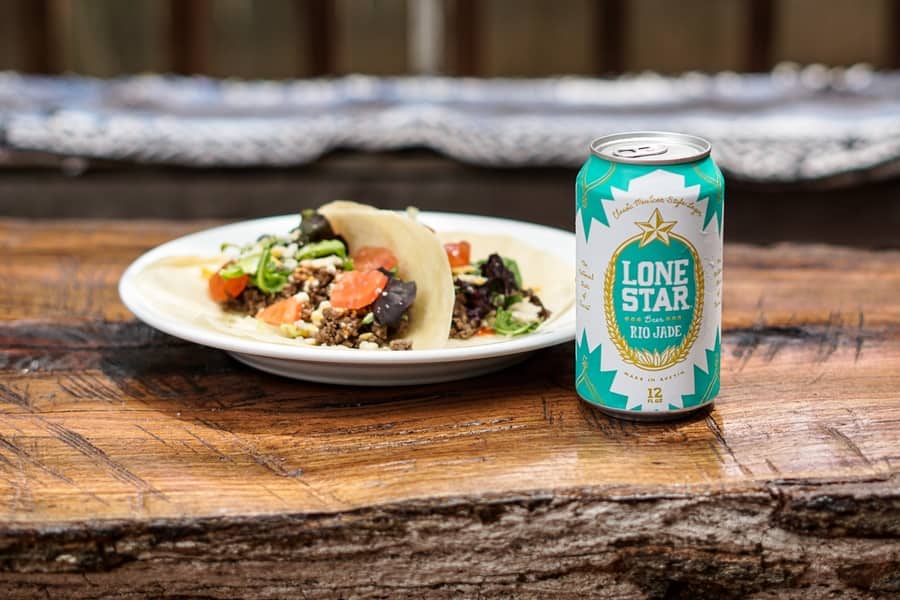 Plate of beef tacos on flour tortillas with a cold Lone Star Rio Jade beer on top of a rustic wood outdoor table