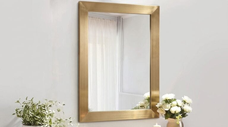Gold-framed mirror reflecting a bright, airy room with white curtains.